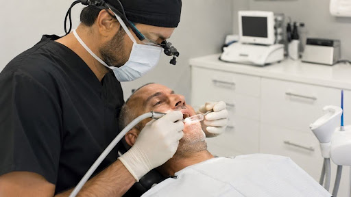 A dentist using surgical loupes and a handpiece during a minimally invasive implant placement procedure.