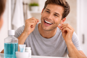 A person flossing their teeth to remove the buildup of plaque on the veneers.