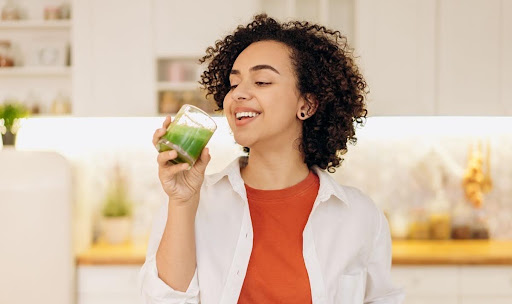 A person smiling while holding a cold green smoothie, one of the recommended soft foods after dental implant surgery.