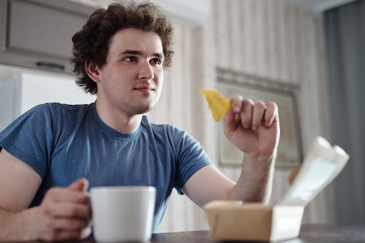  A person holding a crisp and a hot drink, two examples of foods and beverages to avoid after dental implant surgery.