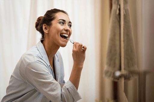 Woman smiling while brushing her teeth as part of a daily dental implant care routine.